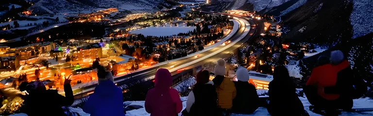people on the edge of a mountain in the winter at night looking at the city